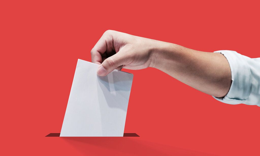 eine Hand steckt einen Wahlzettel in einem Schlitz, der Hintergrund ist rot