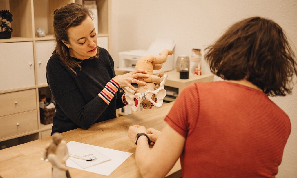 Eine Frau erklärt einer anderen Frau den Geburtsvorgang an Hand eines Modells mit einer Puppe