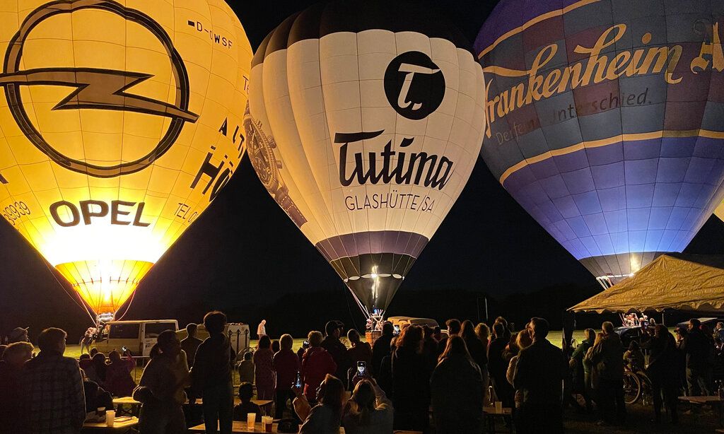drei Heißluftballons in der Nacht, am Boden. Publikum davor