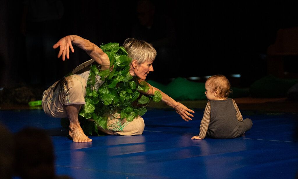 eine mit Efeu behangene Tänzerin kniet neben einem Kleinkind