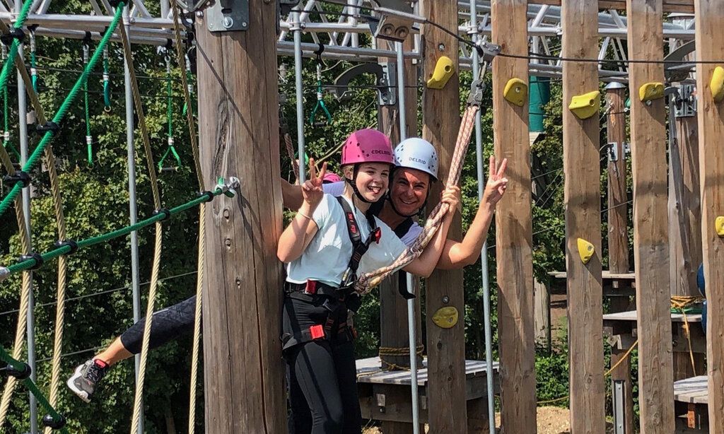 ein Mädchen und eine Frau beim Klettern im Hochseilgarten, zeigen lachend Victory-Zeichen