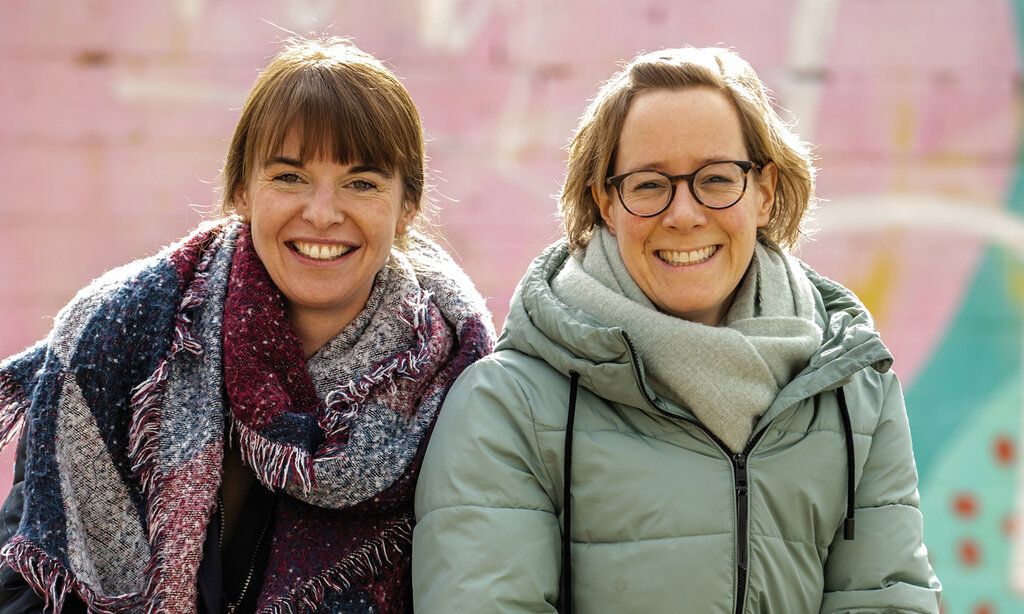Die Gründerinnen der Initiative Kleeblatt Simone Eßer und Eva Schwientek vor einer Mauer, die rosa und türkis angemalt ist