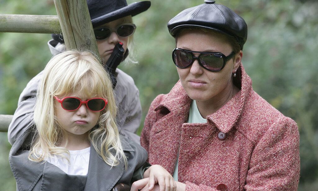 eine Mutter und zwei Kinder gucken grimmig in die Kamera, alle tragen Sonnenbrillen, ein Kind hält eine Spielzeugpistole in der Hand