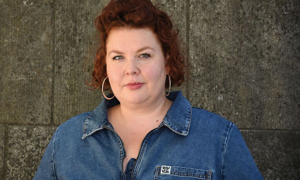 Porträt der Kunstvermittlerin Jana-Catharina Israel vor einer Mauer mit grauen Mauersteinen