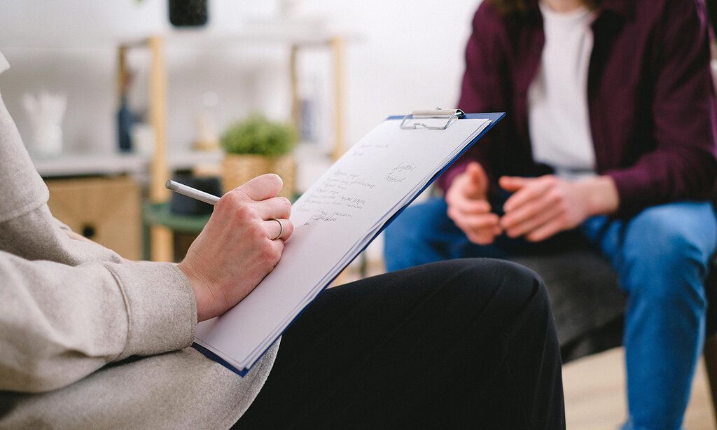 ein Jugendlicher im Beratungsgespräch, im Vordergrund eine Beraterin, die erwas aufschreibt