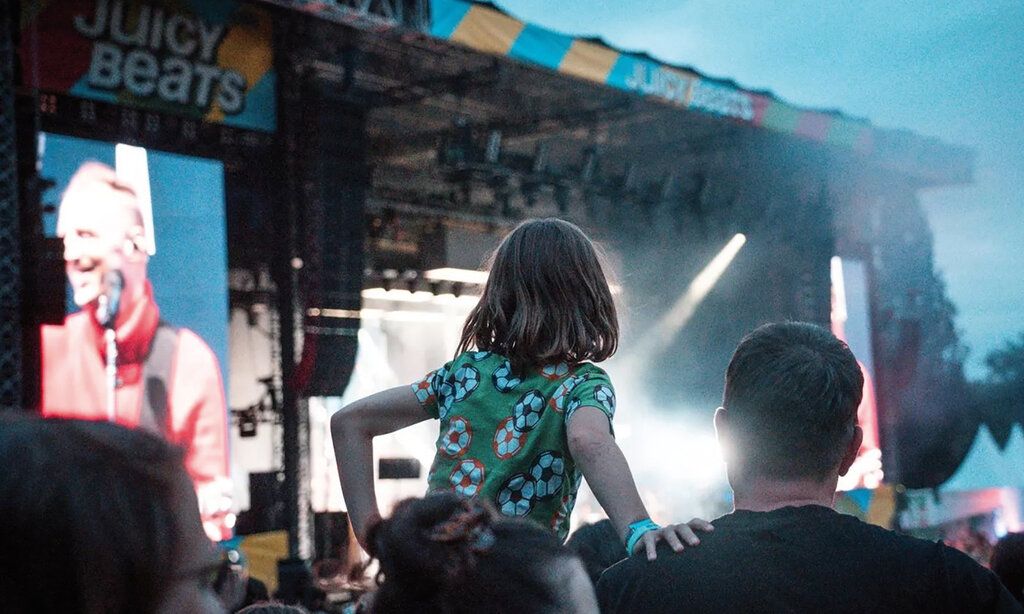 Kind mit Vater im Publikum des Festivals Juicy Beats, im  Hintergrund eine große Bühne