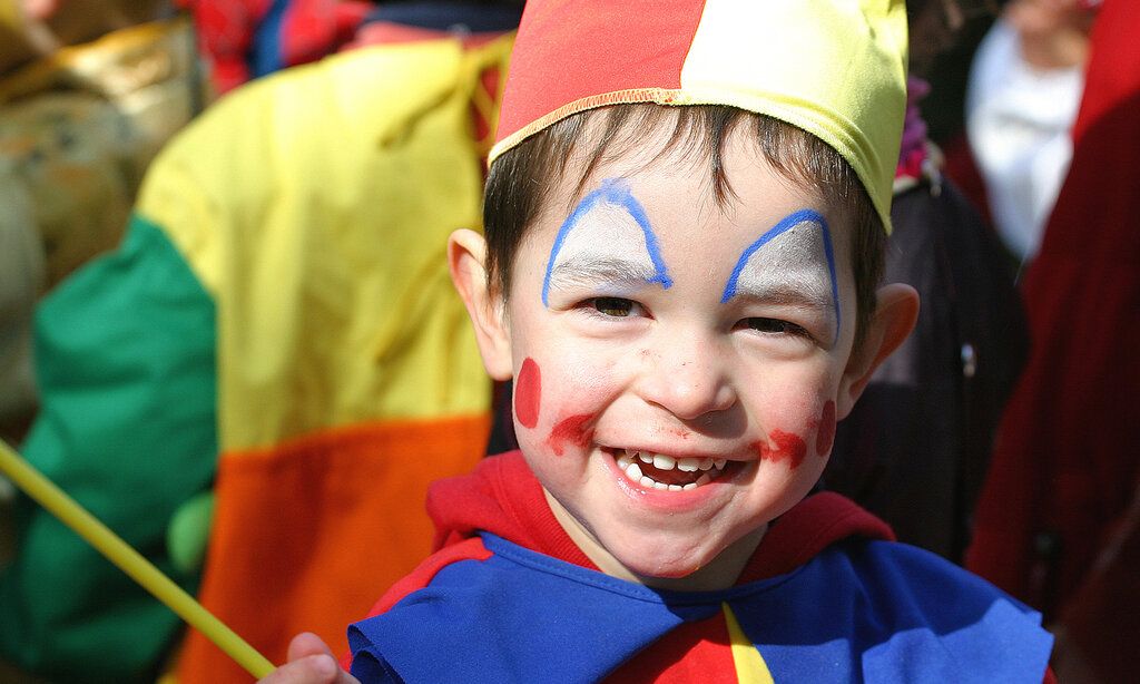 Kleiner Junge, als Clown verkleidet, im Karnevalsgetümmel, lacht in die Kamera
