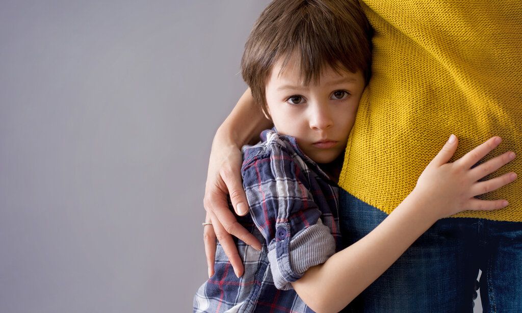 Trauriger Junge schmiegt sich an Mamas Bein