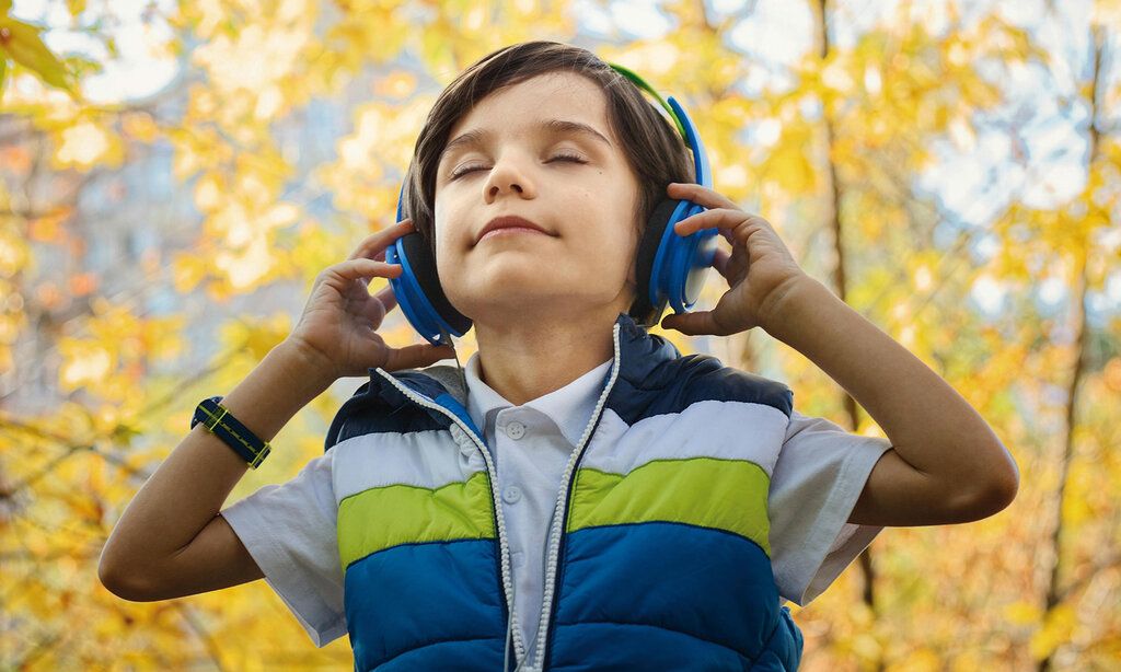 Junge mit Kopfhörern hört Musik, im Hintergrund Herbstlaub