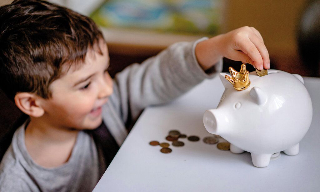 ein kleiner Junge wirft eine Münze ins Sparschwein