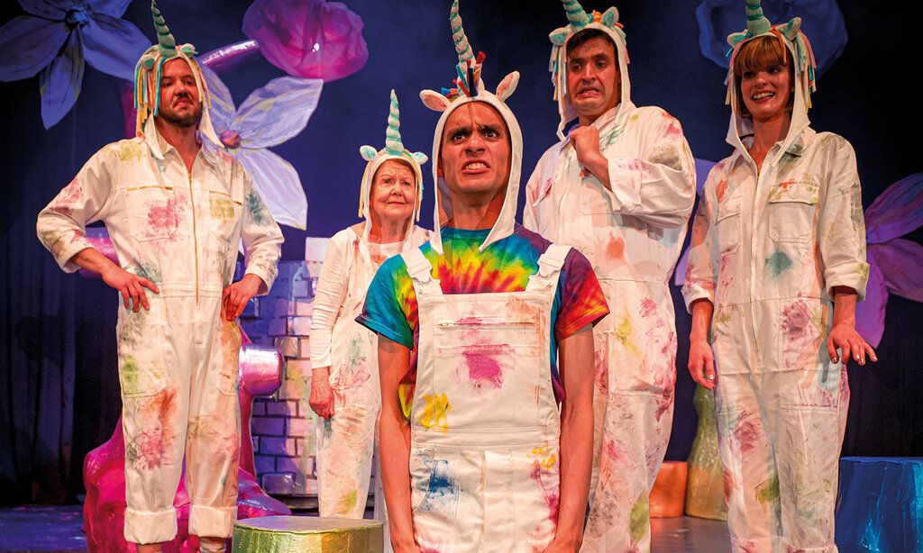 Sechs Schauspieler:innen mit weißen Latzhosen und Einhörnern auf dem Kopf auf Bühne