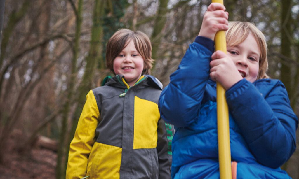Zwei Jungs spielen auf dem Waldspielplatz in Gerresheim, einer hängt an der Seilbahn, winterliche Stimmung