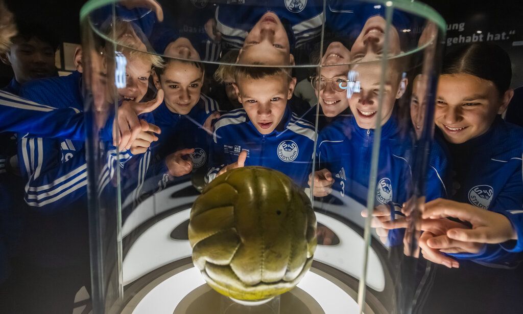 Jungs im Fußballdress betrachten Endspielball von 1954 im Fußballmuseum in Dortmund
