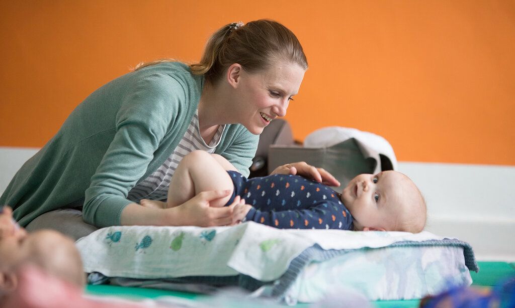 Frau mit Baby beim PeKiP-Kurs, im Hintergrund orange Wand