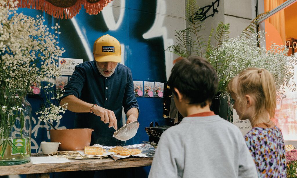 Man bestreut Waffeln mit Puderzucker, Kinder gucken zu