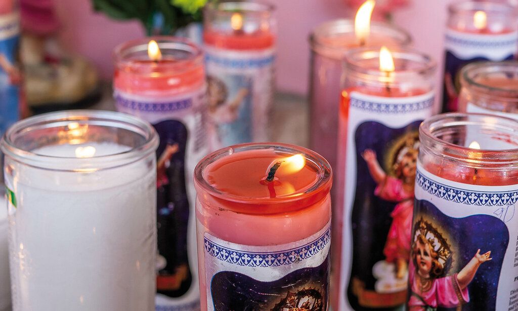 Kerzen in Glasbehältern mit Heiligenmotiven stehen nebeneinander