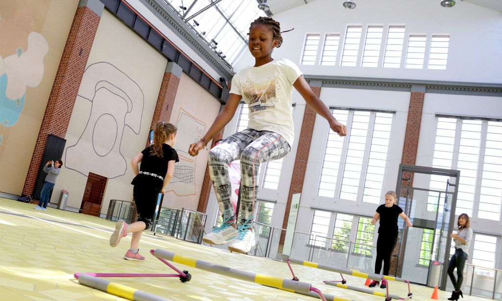 Mädchen springen in einer Turnhalle über kleine Hürden