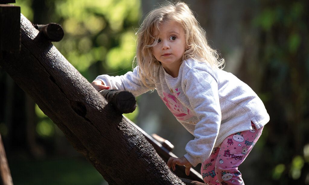 Kind klettert auf ein Holz-Klettergerüst, im Hintergrund unscharfe Bäume
