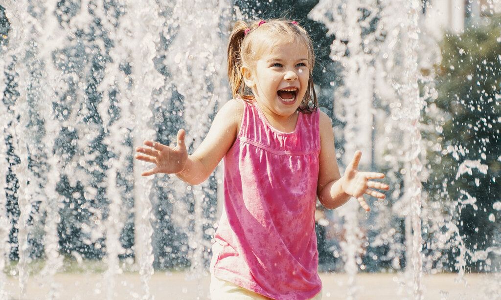 Mädchen steht in Wasserfontänen und lacht