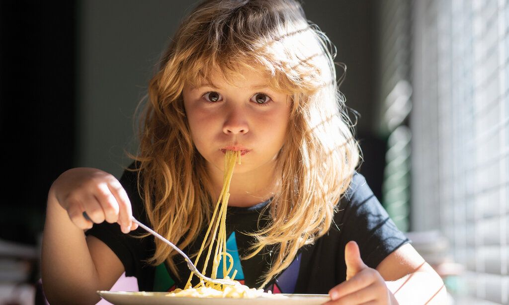 ein Kind isst Spaghetti und guckt in die Kamera