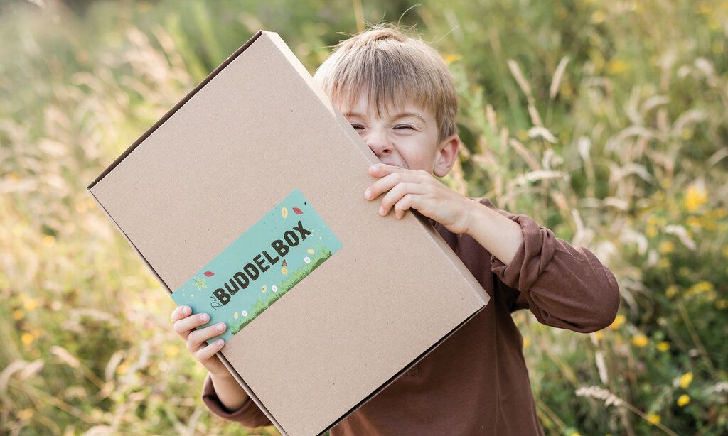 Junge steht auf einer Wiese und hält sich einen Pappkarton vors Gesicht