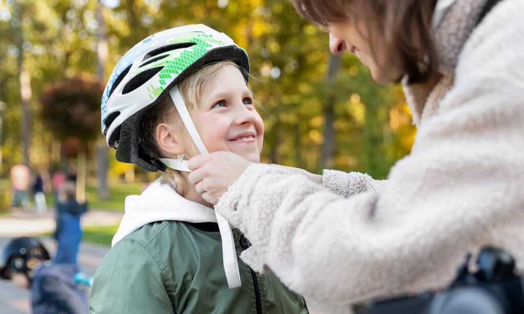 eine Mutter zieht ihrer Tochter einen Fahrradhelm auf, beide lächeln sich an