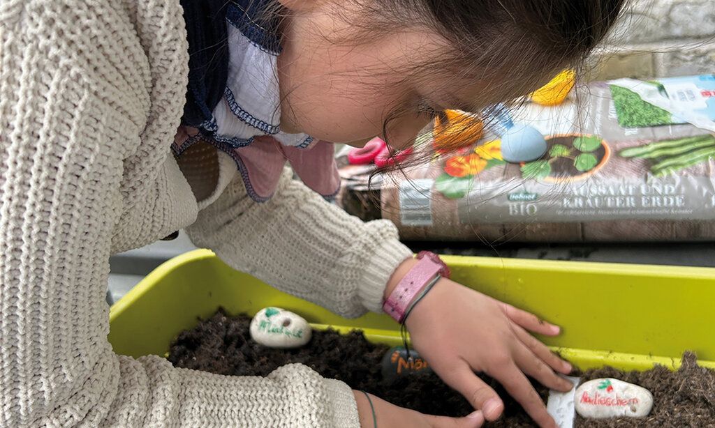 Kind pflanzt etwas in einen Blumenkasten