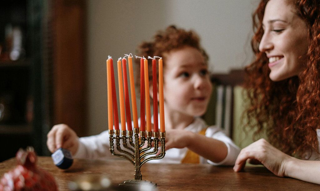 ein achtarmiger Kerzenständer im Vordergrund, dahinter ein Kind mit seiner Mutter an einem Tisch