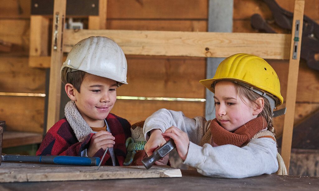 ein Junge und ein Mädchen mit Baustellen-Helmen werkeln mit Hammer in einer Bude im ASP Eller