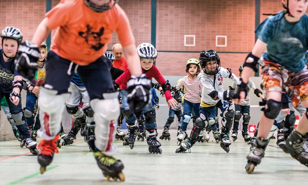 Kinder fahren auf Inlineskates in einer Turnhalle auf den Fotografen zu