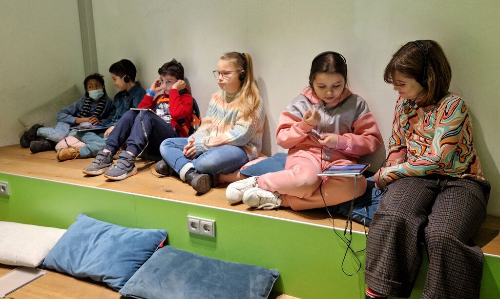 Kinder sitzen auf einem Podest, Düsseldorfer Grundschulkinder bei der Station Kino für die Ohren in der Zentralbibliothek am KAP