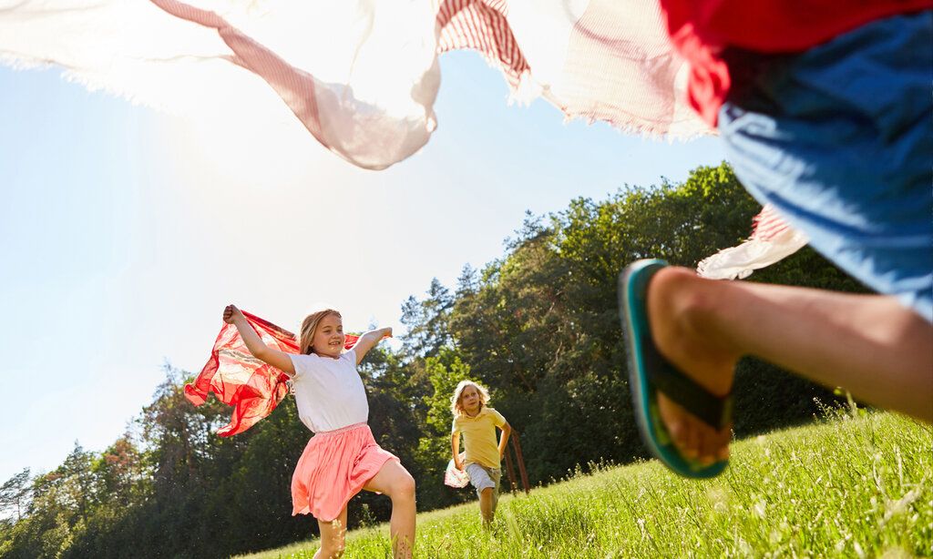 Kinder laufen mit Tüchern über eine Wiese