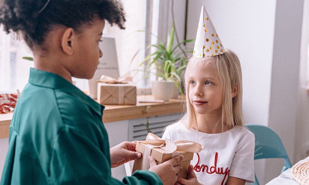 Ein Mädchen mit einem Partyhütchen bekommt von einem anderen Kind ein Geschenk überreicht