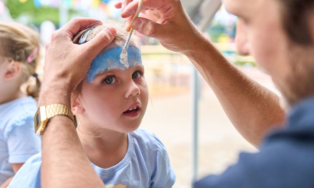 Kinderschminken bei der Einweihung der Kita Flinger Broich, ein Mädchen wird von einem Mann geschminkt
