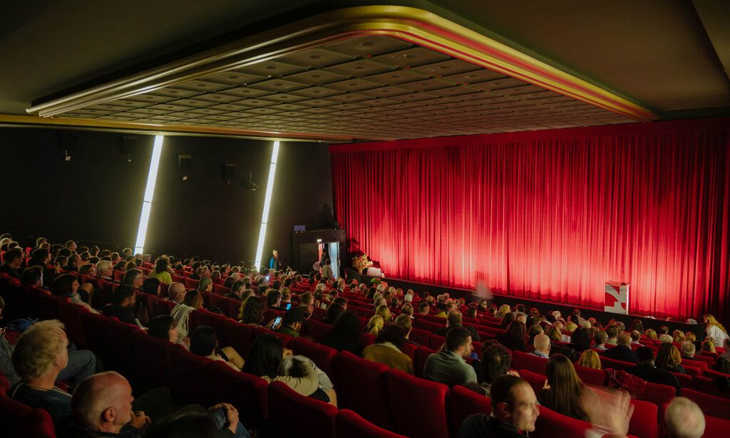 Kinosaal mit Zuschauern während der Kurzfilmtage Oberhausen, roter Vorhang geschlossen
