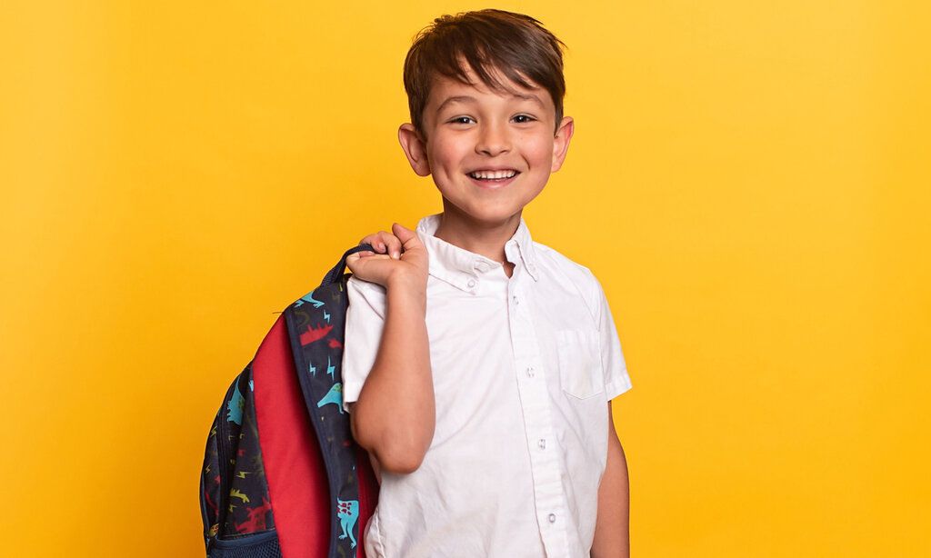 Porträt eines kleinen Jungen mit Schultasche, Hintergrund gelb