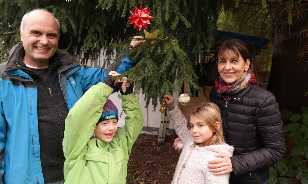 Ein Mann, eine Frau und zwei Kinder stehen bei einer Tanne und schmücken die