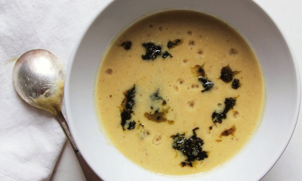 weißer Porzellanteller mit Suppe von oben fotografiert, daneben liegt ein Löffel