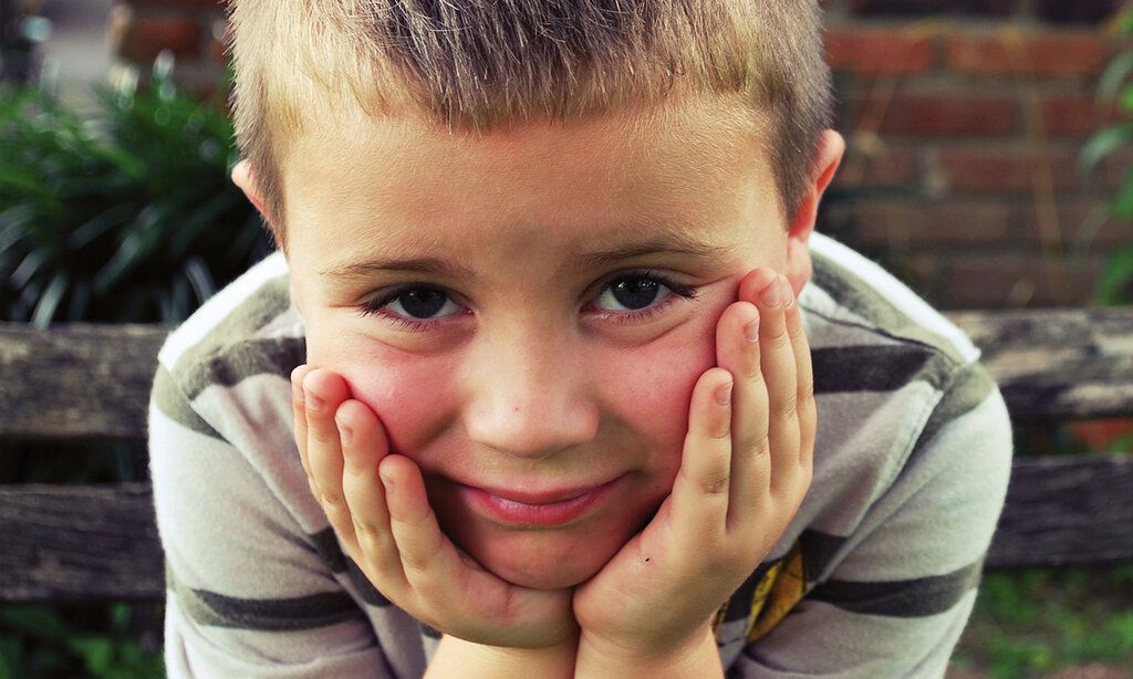 kleiner Junge hat seinen Kopf in die Hände gestützt und schaut in die Kamera