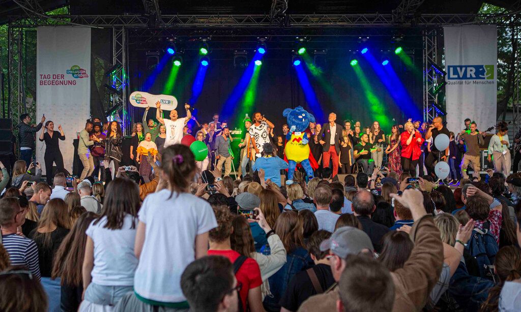 Open-Air-Bühne, auf der sehr viele Menschen singen und tanzen, avor Publikum