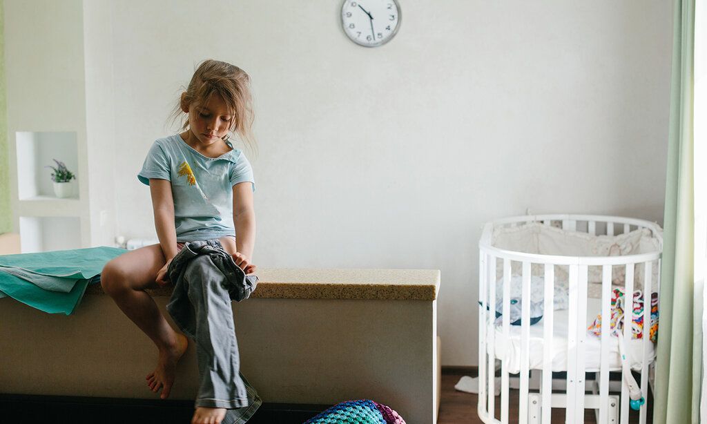 Kleines Mädchen sitzt im Kinderzimmer, zieht sich selbst ihre Hose an.