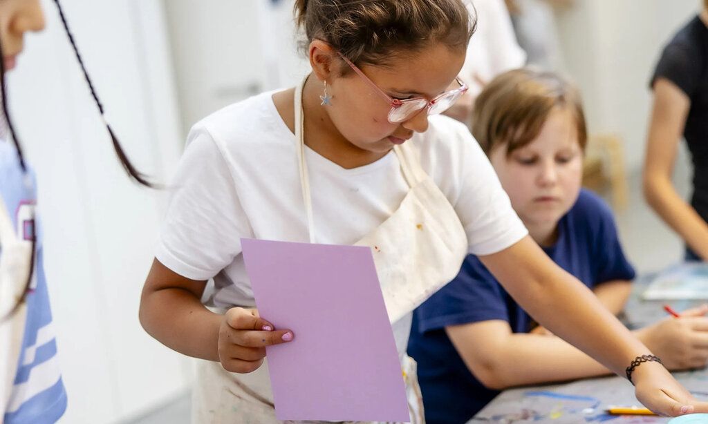 Mädchen arbeitet in Druckwerkstatt, andere Kinder gucken zu