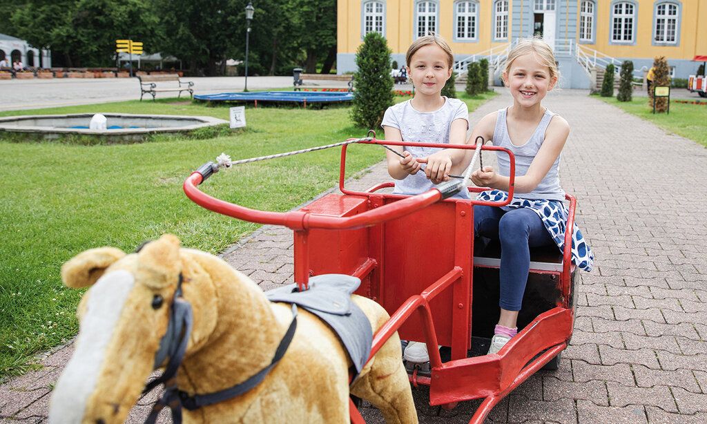 Zwei Mädchen in einer Kutsche mit Plüschpferd, im Hintergrund Schloss Beck