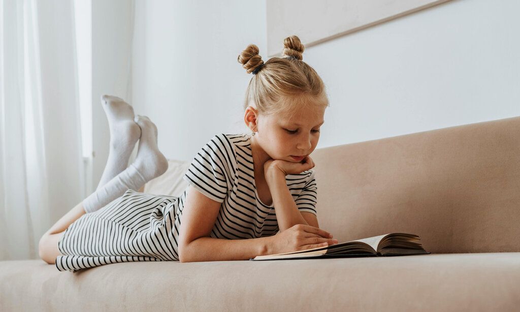 ein Mädchen liegt bäuchlings auf einem Sofa und liest in einem Buch
