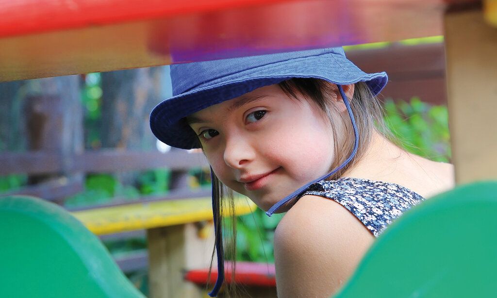 Porträt, Mädchen mit Down Syndrom guckt durch ein Klettergerüst auf einem Spielplatz