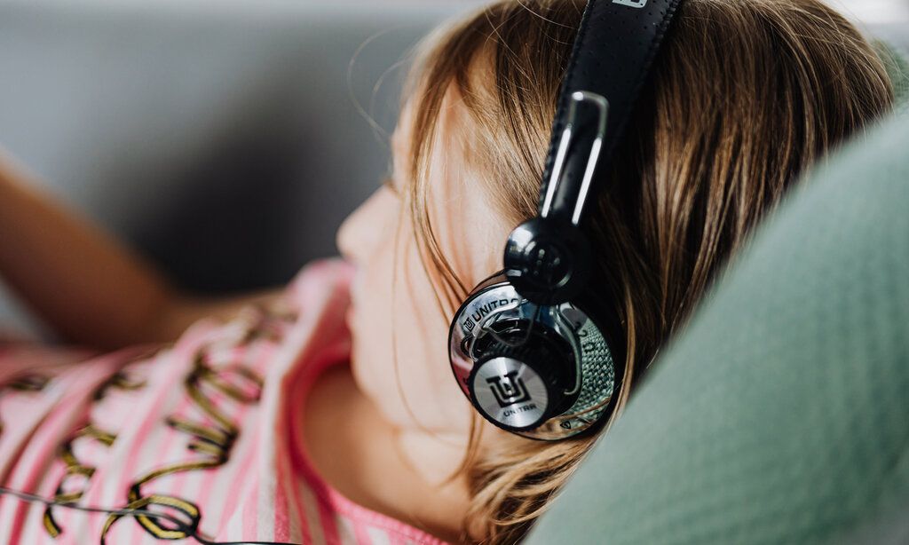 Mädchen liegt mit Kopfhörern auf einem Kissen, das Mädchen ist unscharf, der Kopfhörer scharf