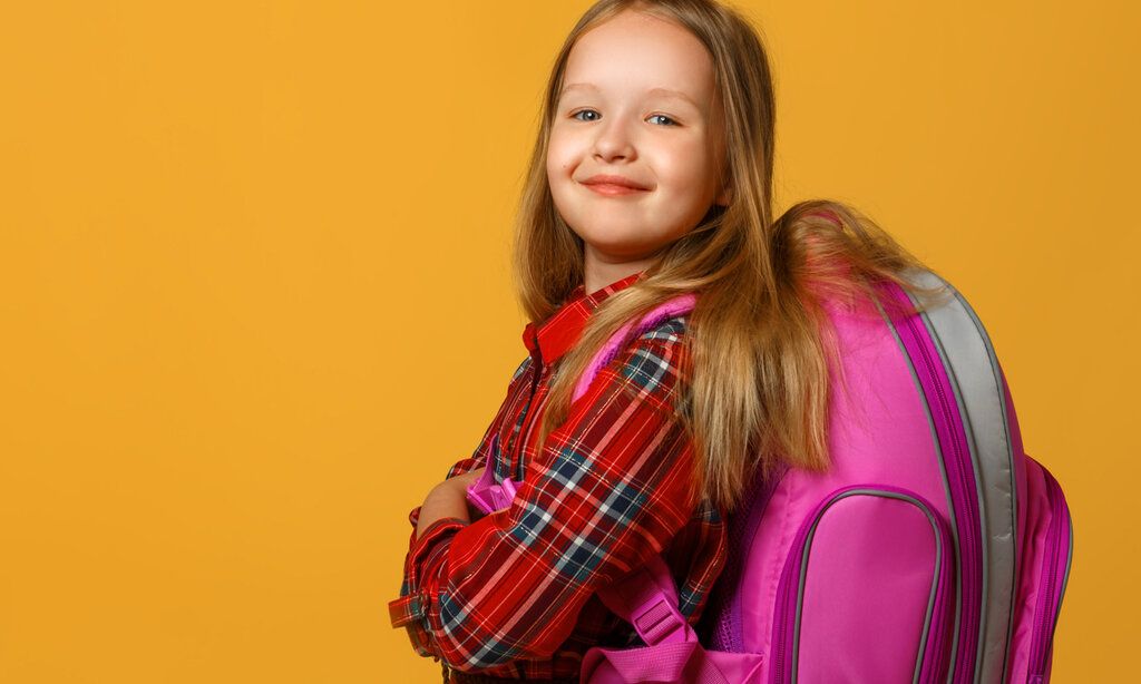 Mädchen mit kariertem Hemd und pinkem Tornister vor orangem Hintergrund