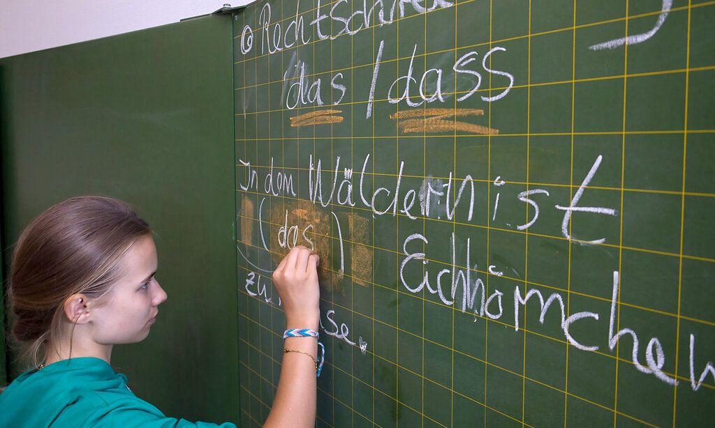 Mädchen schreibt mit Kreide an eine  Schultafel