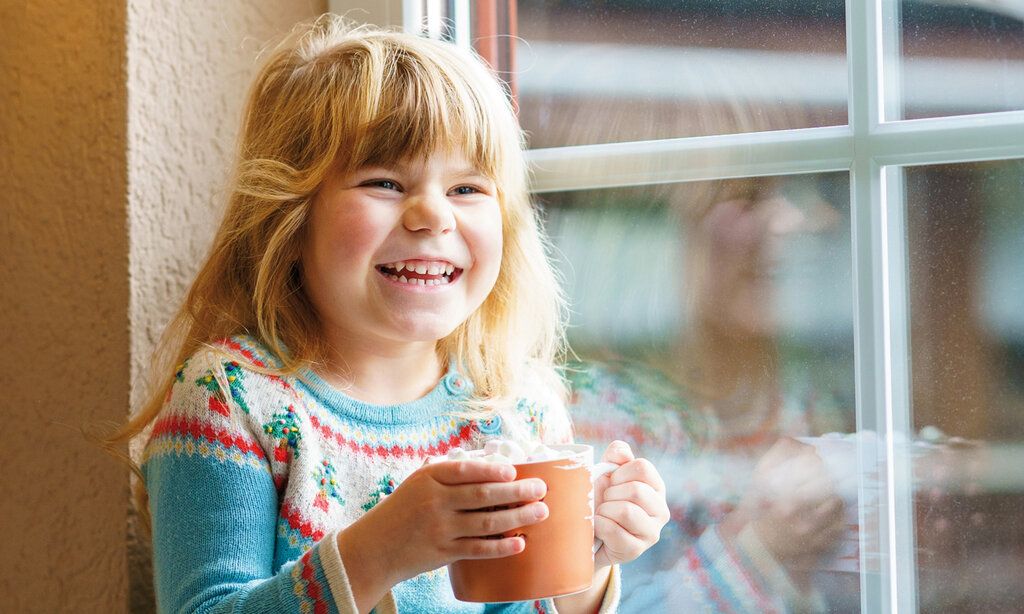 Mädchen sitzt mit Tasse am Fenster und lacht