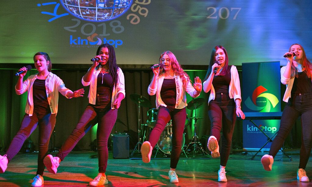 Fünf Mädchen tanzen und singen auf einer Bühne